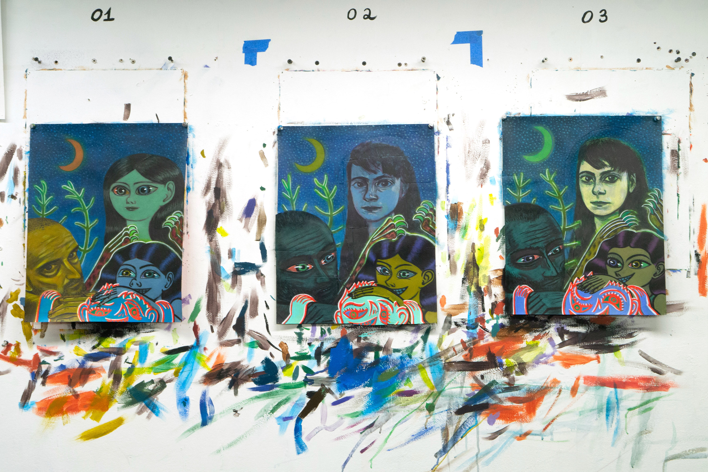 Three paintings on a paint-splattered studio wall